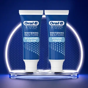 Two tubes of Oral-B 3D White Clinical Whitening Restore toothpaste, one labeled Diamond Clean and the other Power Fresh, stand on a reflective surface against a blue background with a glowing arch.