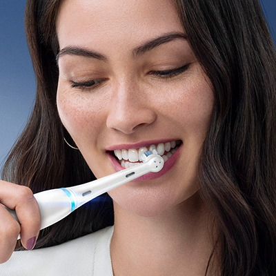 Oral-B electric toothbrush in use, demonstrating its cleaning action on a woman's teeth.