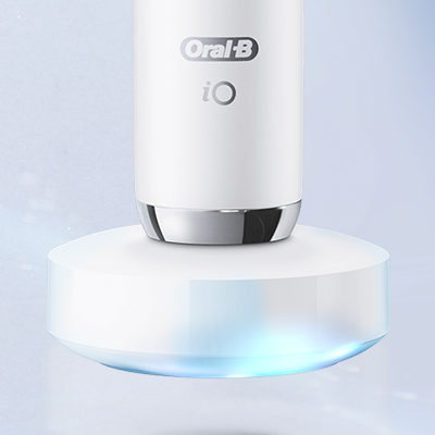Oral-B iO toothbrush charging on its base, with a glowing blue light underneath.