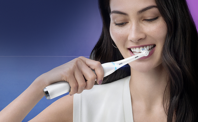 Oral-B electric toothbrush in use, woman smiling while brushing her teeth.