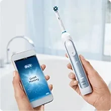 Hands holding a smartphone displaying Oral-B logo and Good Morning, next to an electric toothbrush.