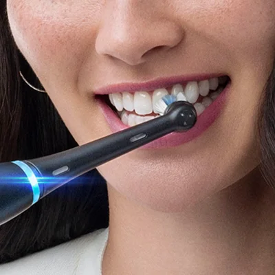 Oral-B electric toothbrush in use, demonstrating its cleaning action on a woman's teeth.