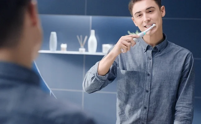 Oral-B electric toothbrush in use, demonstrating a clean and healthy smile in a modern bathroom setting.