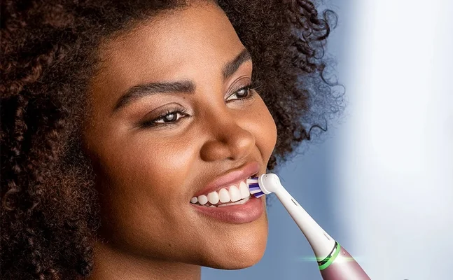 Oral-B electric toothbrush being used by a smiling woman, highlighting the benefit of clean, white teeth.