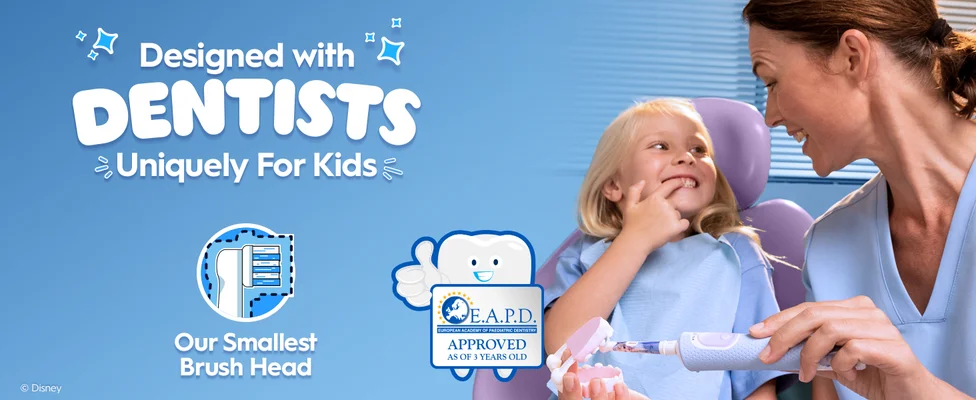 A dentist helps a young child brush with a blue electric toothbrush featuring a Frozen design. Text: “Designed with Dentists, Uniquely for Kids” and “Our Smallest Brush Head.”