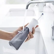 Hand filling a portable water flosser under a running tap in a white sink.