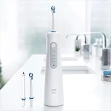A white electric water flosser and two tips are on a bathroom counter, with visible text GENTLE MEDIUM INTENSE.