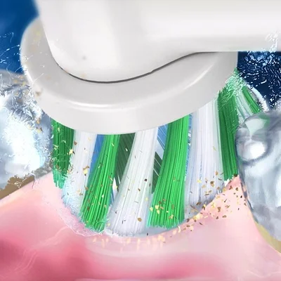 Oral-B toothbrush head cleaning teeth, showing green, white, and blue bristles removing plaque and debris.