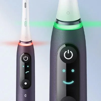 Oral-B iO toothbrush showing pressure sensor light in red and green, and a smiley face on the display.