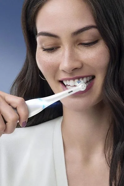 Oral-B electric toothbrush in use, demonstrating its cleaning action on a woman's teeth.