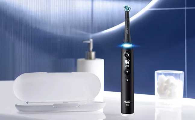 Oral-B iO toothbrush in black, standing upright next to its open travel case and a container of cotton balls.