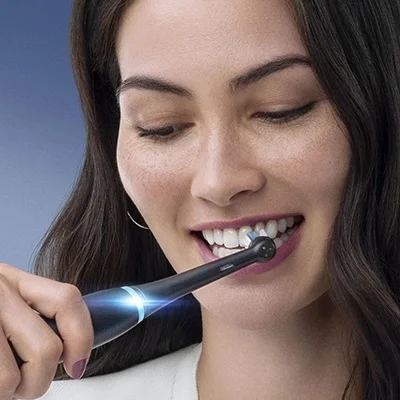 Oral-B electric toothbrush being used by a woman, showcasing its cleaning action and illuminated handle.