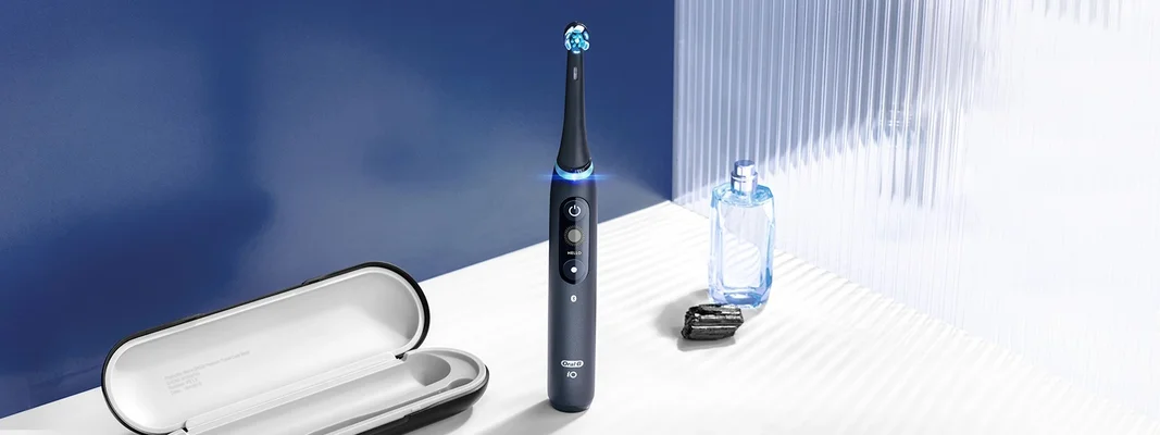 Oral-B iO toothbrush displayed with travel case, perfume bottle, and a dark stone on a white surface.
