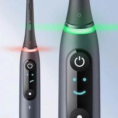 Oral-B iO toothbrush showing red and green light indicators, and a smiley face on the display.