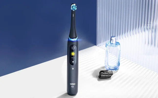 Oral-B iO toothbrush, showcasing the interactive display and sleek design, next to a perfume bottle.