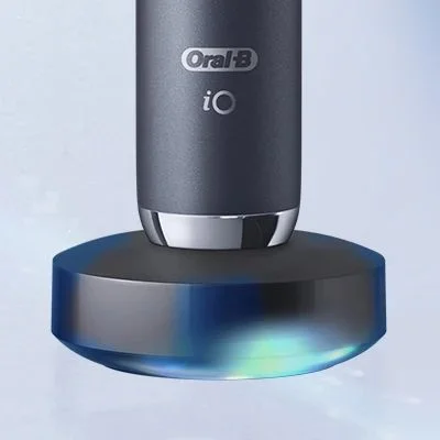 Oral-B iO toothbrush charging on its magnetic base, which is illuminated with a soft blue light.