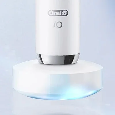 Oral-B iO toothbrush charging on its base, with a subtle blue light emanating from underneath.