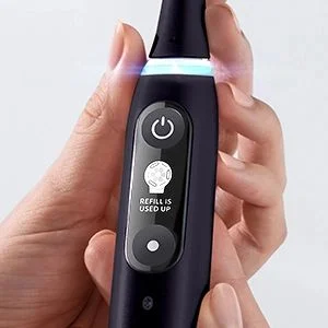 Oral-B toothbrush displaying a notification that a refill is needed, held in someone's hand.