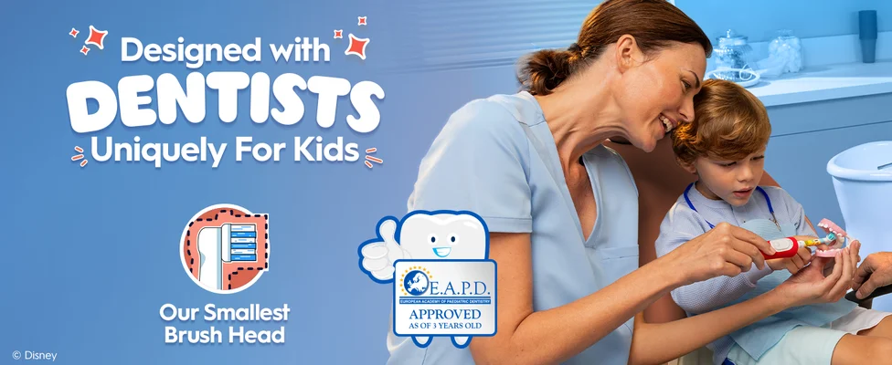 A female dental professional is showing a young boy how to use an Oral-B electric toothbrush on a model of teeth. Text reads "Designed with Dentists - Uniquely for Kids". Icons show a small brush head and an E.A.P.D. (European Academy of Paediatric Dentistry) approval badge for ages 3+.
