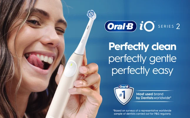 A woman smiles and sticks out her tongue while holding a white Oral-B iO Series 2 electric toothbrush, with the text Perfectly clean perfectly gentle perfectly easy and an Oral-B logo featuring #1 Most used brand by Dentists worldwide.