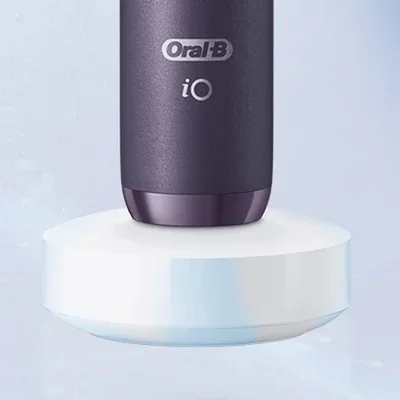 Oral-B iO electric toothbrush in dark purple resting on its white magnetic charging base.