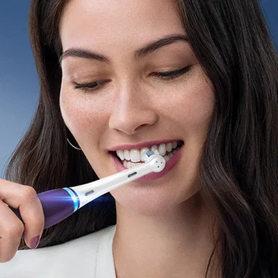 Oral-B electric toothbrush in use, showing a woman brushing her teeth with the round brush head.