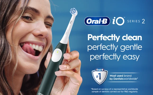 A woman smiles and sticks out her tongue while holding a white Oral-B iO Series 2 electric toothbrush, with the text Perfectly clean perfectly gentle perfectly easy and an Oral-B logo featuring #1 Most used brand by Dentists worldwide.