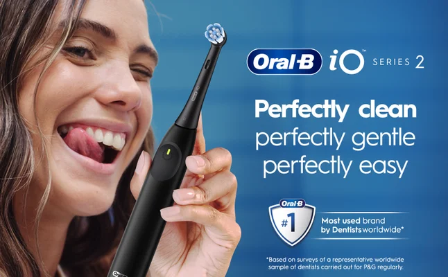 A woman smiles and sticks out her tongue while holding a white Oral-B iO Series 2 electric toothbrush, with the text Perfectly clean perfectly gentle perfectly easy and an Oral-B logo featuring #1 Most used brand by Dentists worldwide.