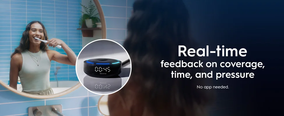 A woman smiles while brushing her teeth in a bathroom mirror reflection, next to a device displaying 00:45 and the text iO sense, with overlay text that reads Real-time feedback on coverage, time, and pressure No app needed.