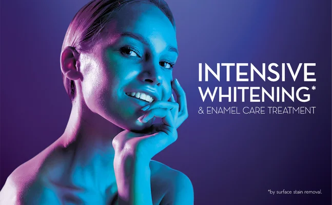 Woman smiling with purple and blue light on her face with text that says INTENSIVE WHITENING* & ENAMEL CARE TREATMENT *by surface stain removal.